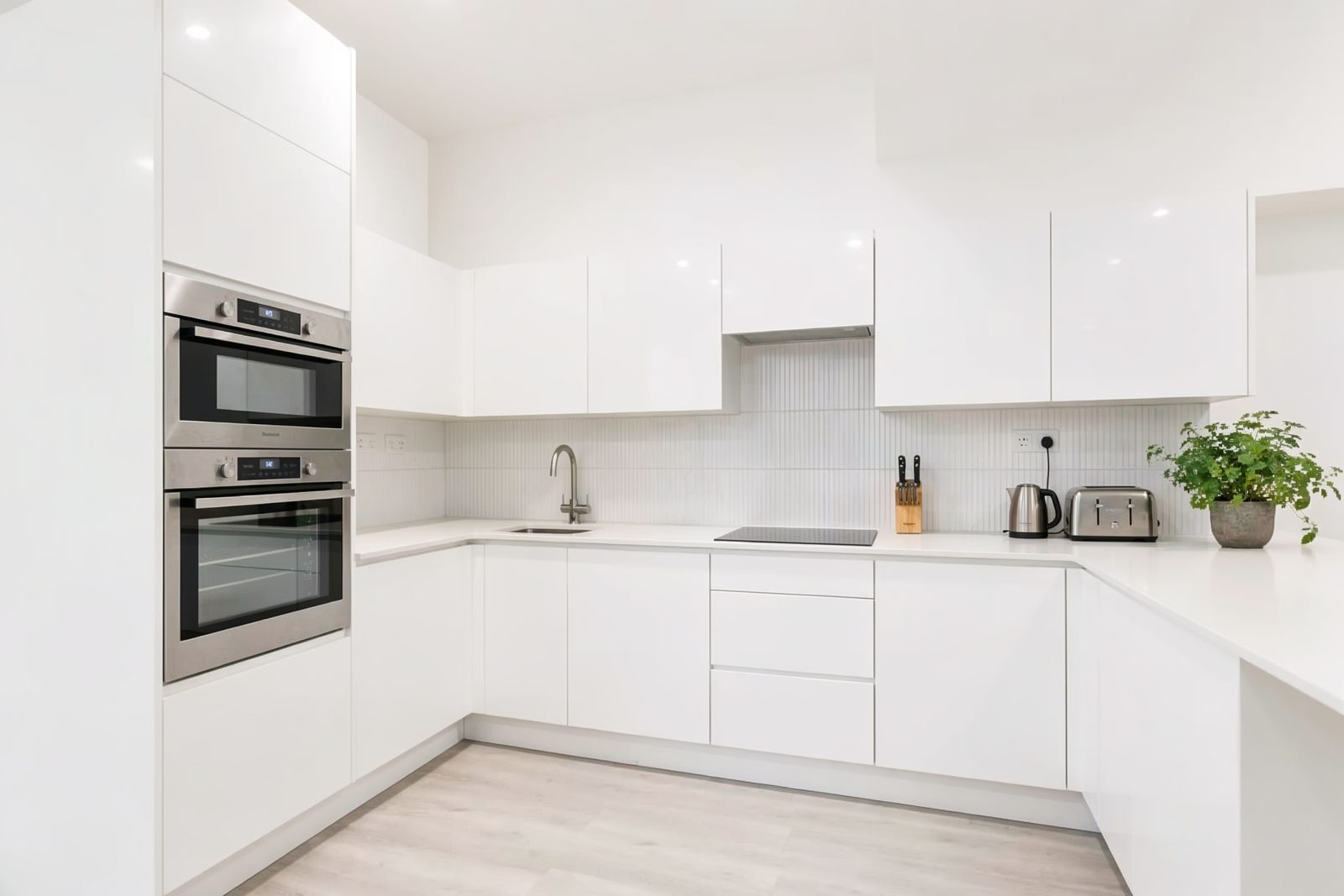 White kitchen with a built-in double oven, pale tiled splashback and white worktops.