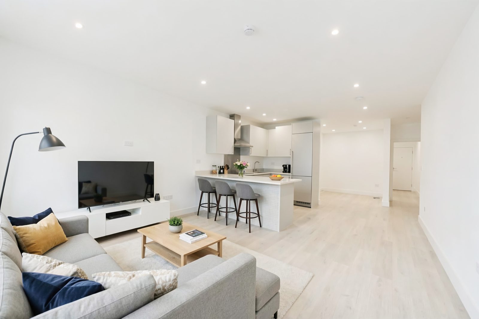 Open-plan kitchen and living area of the completed apartment, with a grey sofa, a breakfast bar with three stools and a pale wood floor.